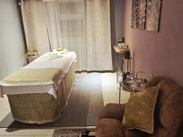 Cozy Thai massage room with treatment bed, brown chair, and soft curtains