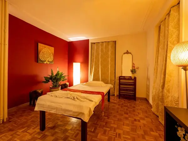 Warm massage room with treatment table, red walls, and soft curtains