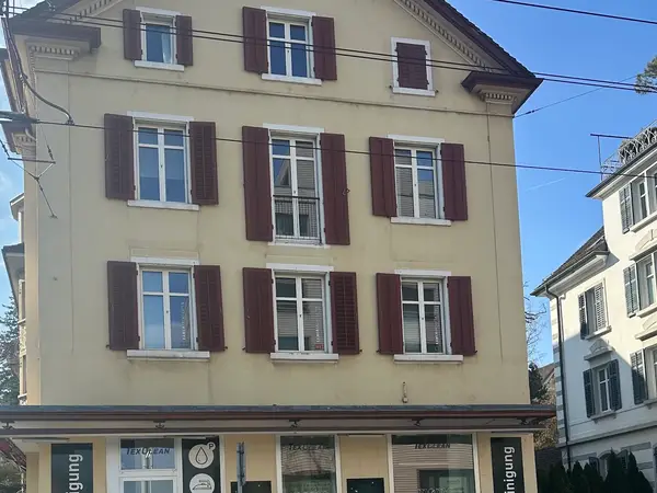 Street-facing beige building with maroon shutters under a clear blue sky