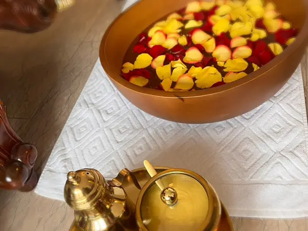 Golden spa tray with flower petals and ornate brass tea service on a white towel