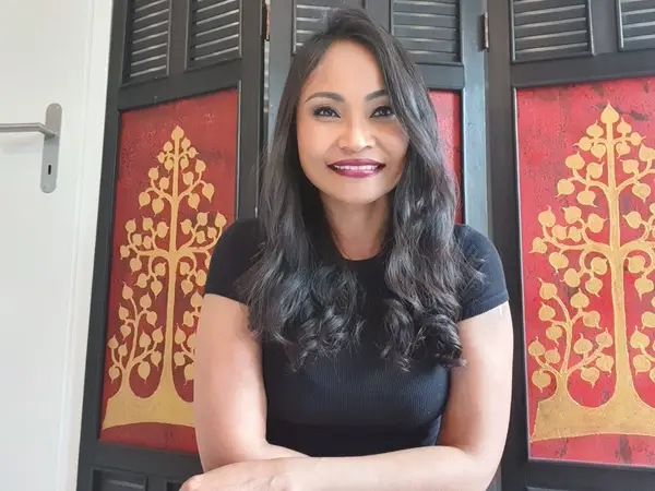 Smiling woman standing before red-and-gold decorative panels indoors