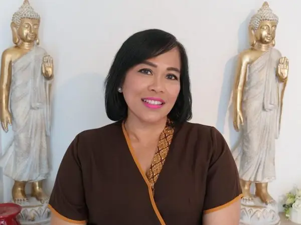 Woman in brown Thai massage uniform between two Buddha statues