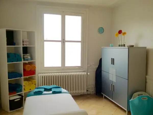 Bright massage room with treatment table, towel shelves, cabinet, and window