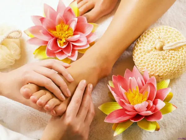 Hands massaging a foot with pink lotus flowers and spa decor