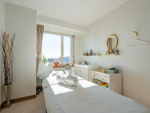 Bright massage room with treatment bed, white decor, and window view