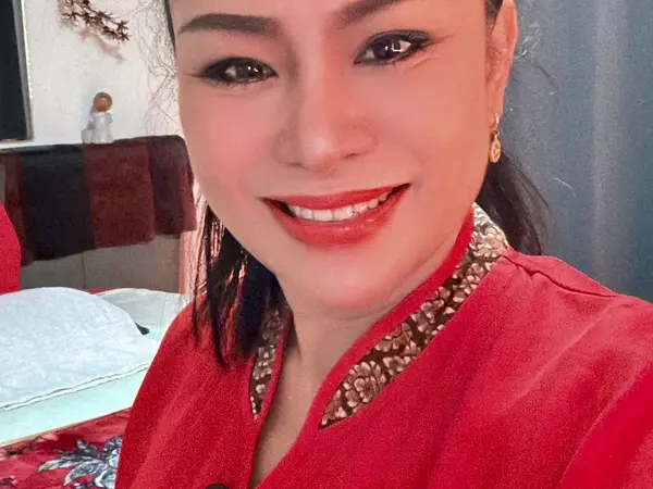 Smiling woman in red uniform beside a massage bed in a cozy room