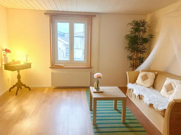 Bright massage room with sofa, table, window, and warm lighting