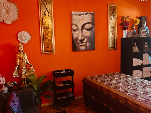 Bright orange massage room with Buddha decor and a patterned treatment bed