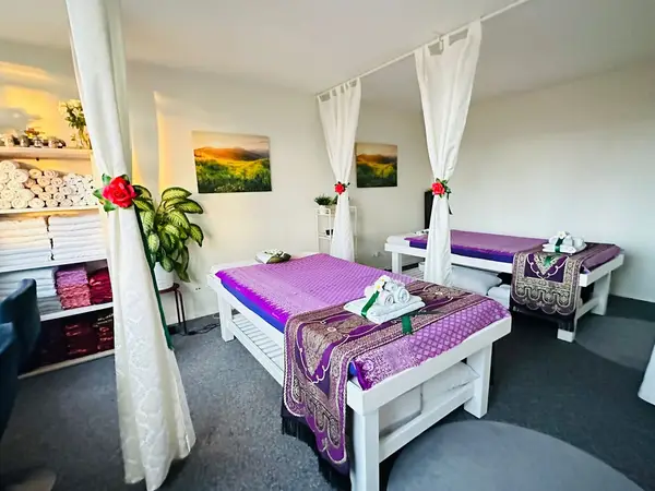 Bright massage room with two treatment tables, purple linens, and white curtains