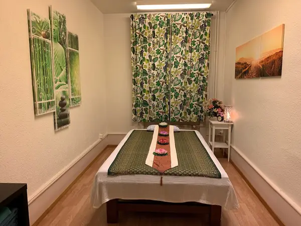 Thai massage treatment room with massage table, floral curtains, and wall art