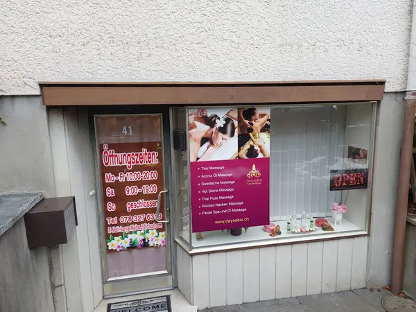 Street-level Thai massage storefront with window signs, open neon, and pink decor