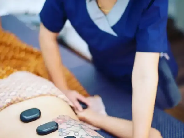 Massage therapist working on a client with hot stones on a treatment bed