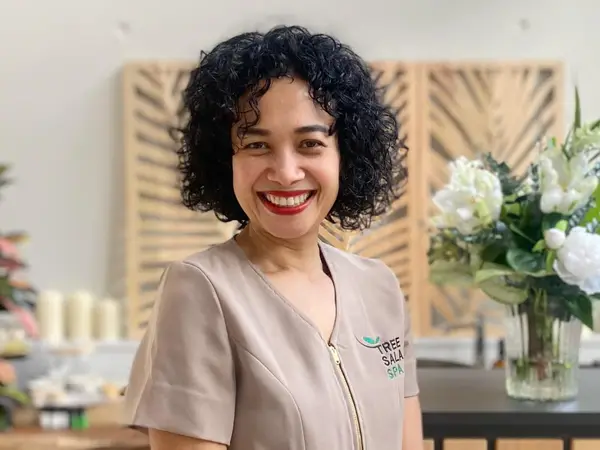 Smiling spa staff member in a bright reception area with flowers and wooden decor