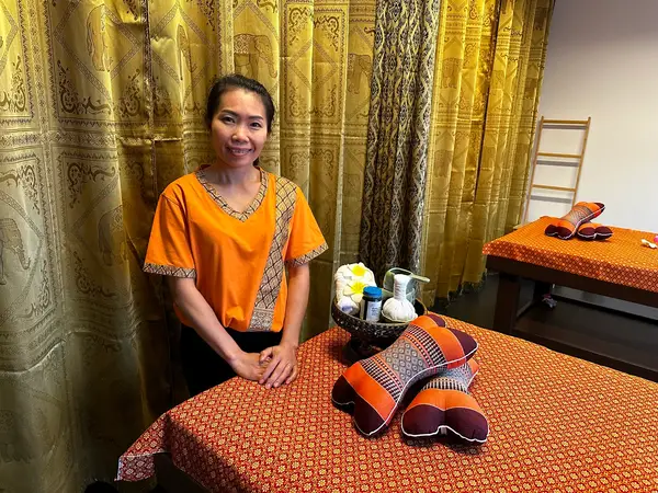 Thai massage room with ornate curtains, orange bedding, and a smiling therapist