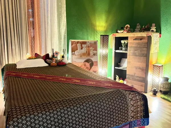 Cozy Thai massage room with bed, green wall, shelves, and decorative lamps