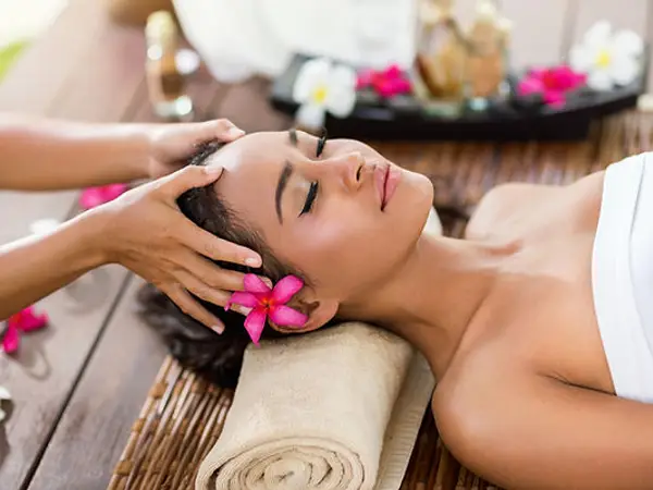 Woman receiving a head massage with flowers in a serene spa room