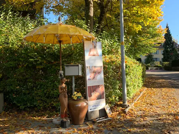 Exterior sidewalk display with yellow umbrella, statue, and spa banner amid autumn foliage