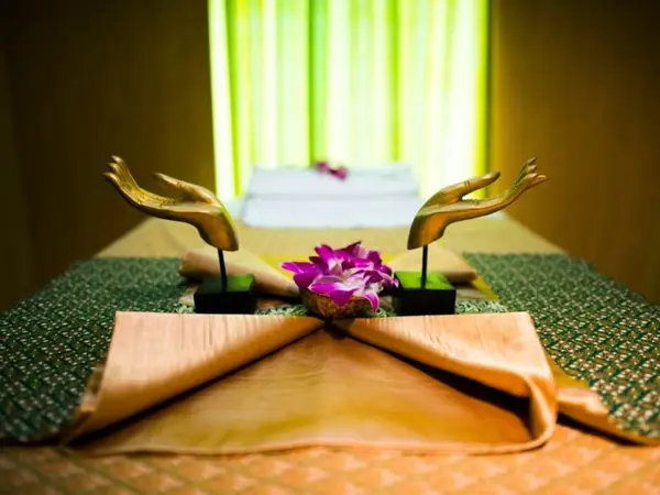 Massage room with neatly arranged bed, purple flowers, and gold hand statues