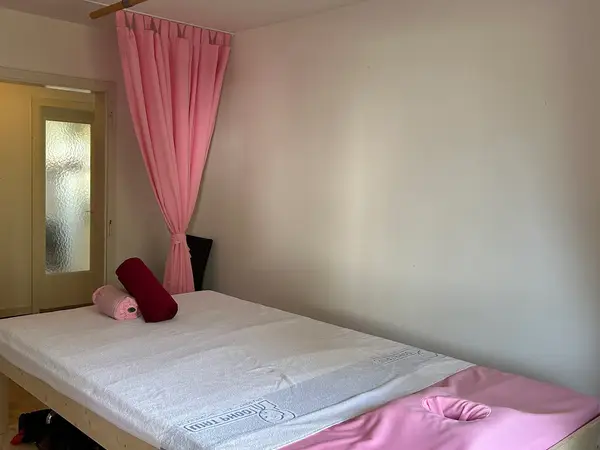 Minimal massage room with bed, pink curtains, and frosted door