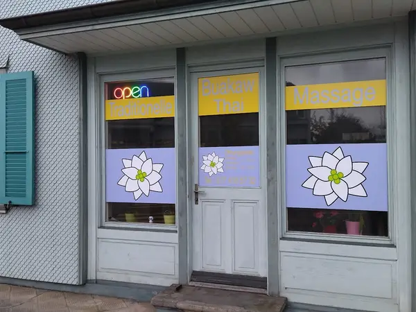Exterior storefront of Buakaw Thai Massage with lotus window decals and open sign