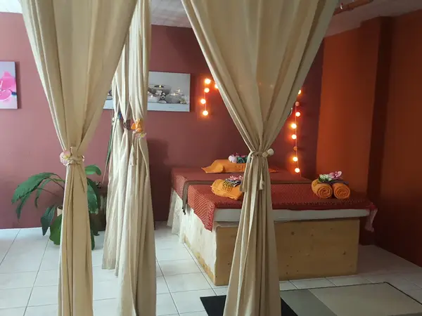 Curtained Thai massage room with bed, red walls, and warm lights