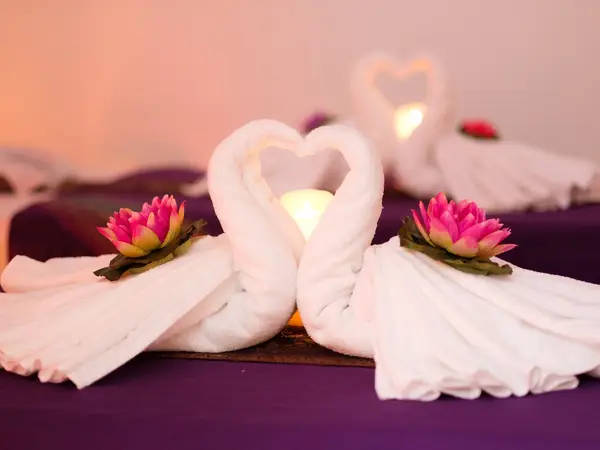 Spa massage bed with folded towels, lotus flowers, and candlelit heart decor