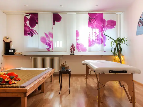 Bright massage room with two tables, orchid window panels, and a potted plant