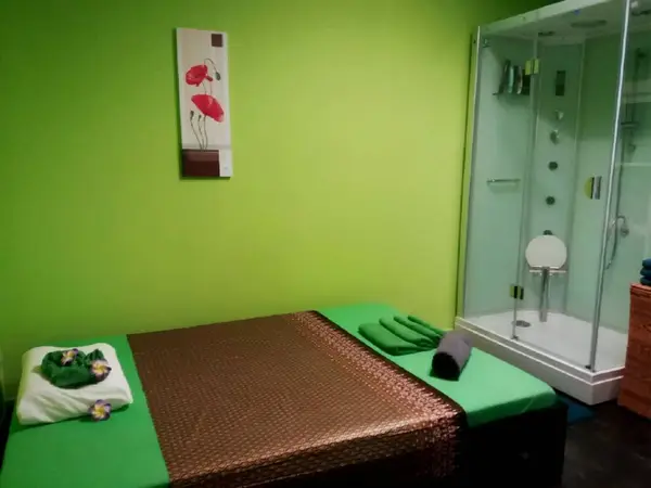 Green massage room with mat, towel, and glass shower stall