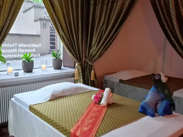 Thai massage room with two beds, gold curtains, candles, and potted plants