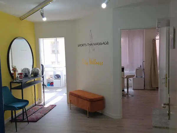 Bright massage salon reception with yellow accent wall, mirror, bench, and open doorway rooms