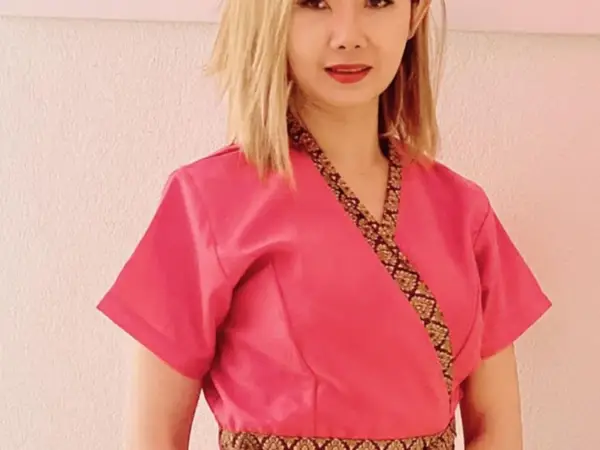 Woman in pink Thai-style uniform against a plain light wall