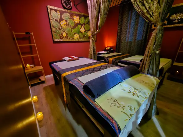 Cozy massage room with three beds, curtains, warm lighting, and red walls
