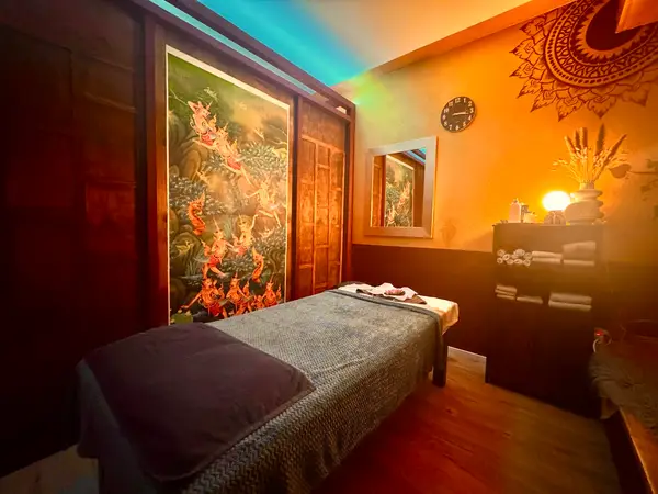 Warm Thai massage room with a treatment bed, wall art, and soft lighting