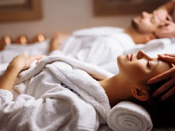 Two clients receive facial massage in a softly lit spa room