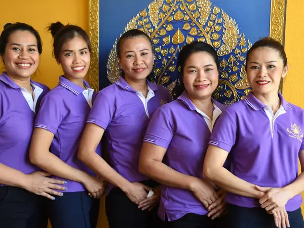 Five smiling women in purple uniforms stand before ornate blue-and-gold decor