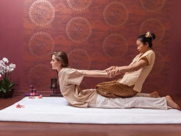 Two women in a Thai massage room with a red patterned wall