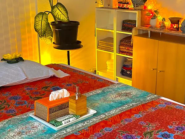 Warm Thai massage room with patterned treatment bed, shelves, cabinets, and plants