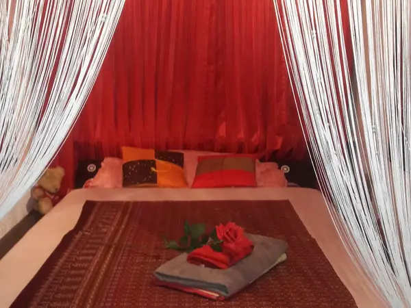 Red-draped massage bed with white beaded curtains and folded towels