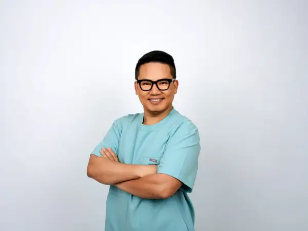 Smiling therapist in teal scrubs against a plain white background
