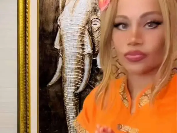 Blonde woman in orange uniform before framed elephant artwork inside a salon