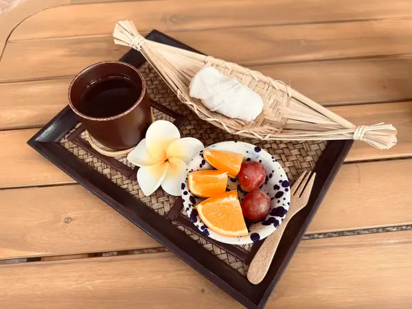 Tray with tea, fruit, and a woven decorative object on a wooden table