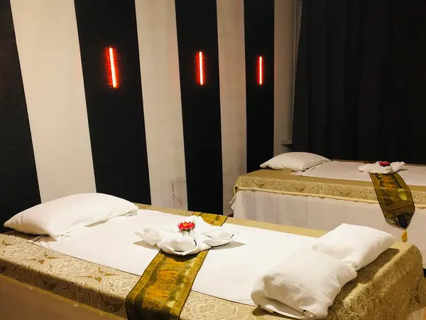Massage room with two neatly made treatment beds and dim red wall lights