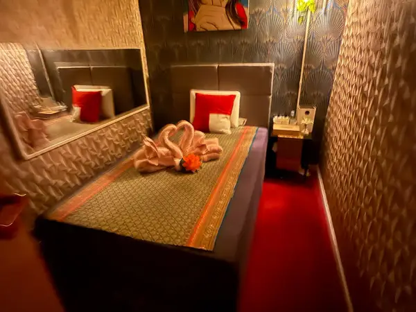 Thai massage room with patterned walls, red carpet, and neatly made bed