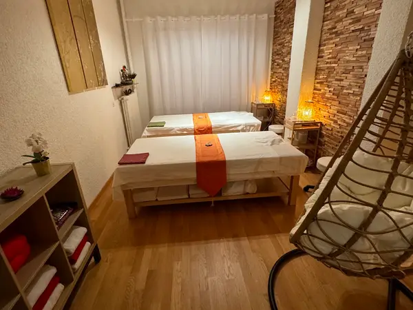 Warm Thai massage room with two treatment tables, lamps, and woven chair
