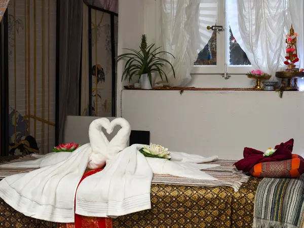 Thai massage room with heart-shaped towels, white drapes, and a decorated table