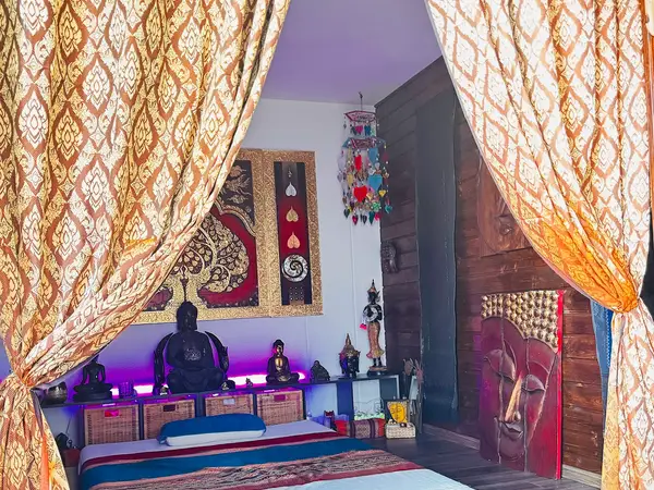 Thai massage room with draped curtains, Buddha statues, and purple accent lighting