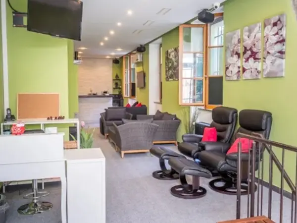 Bright massage salon waiting area with green walls, sofas, and black recliners