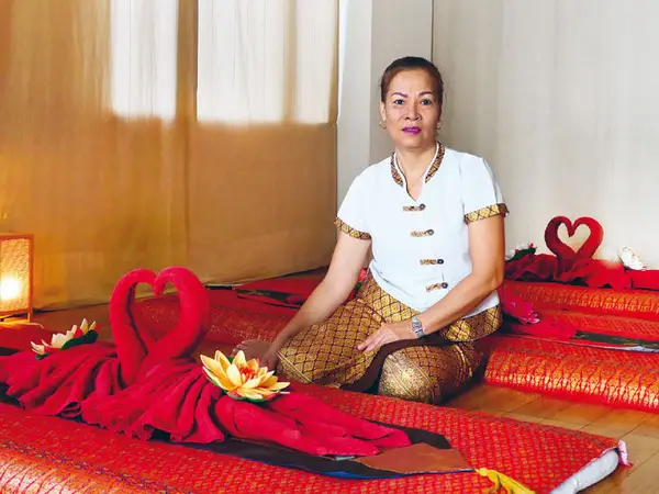 Thai-massage room with red mats, folded towels, and a seated therapist