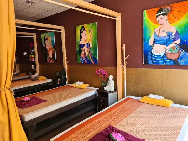 Thai massage room with two beds, colorful wall art, and warm decor