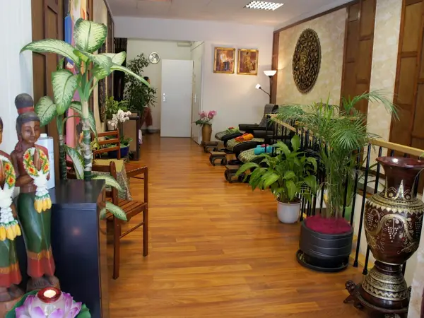 Bright massage salon hallway with wooden floor, plants, Thai decor, and chairs